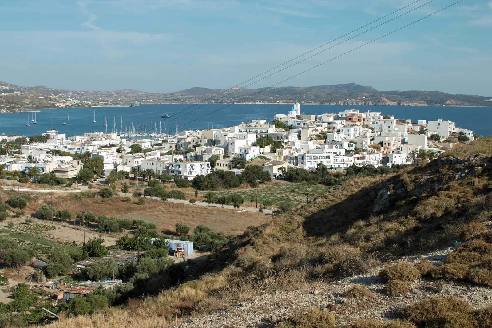 Adamas seen from a hill above town, with white houses, the marina with sailing boats and the bay of Milos behind