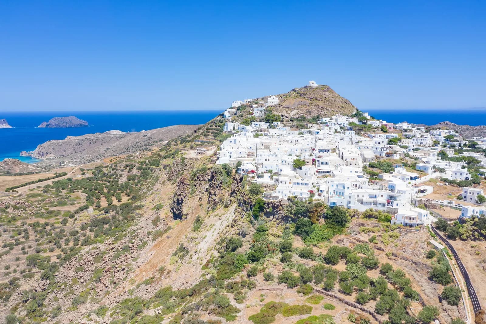 Aerial view of the white houses of Plaka on a ridge above the sea, with the castle hill and its chapel at the top