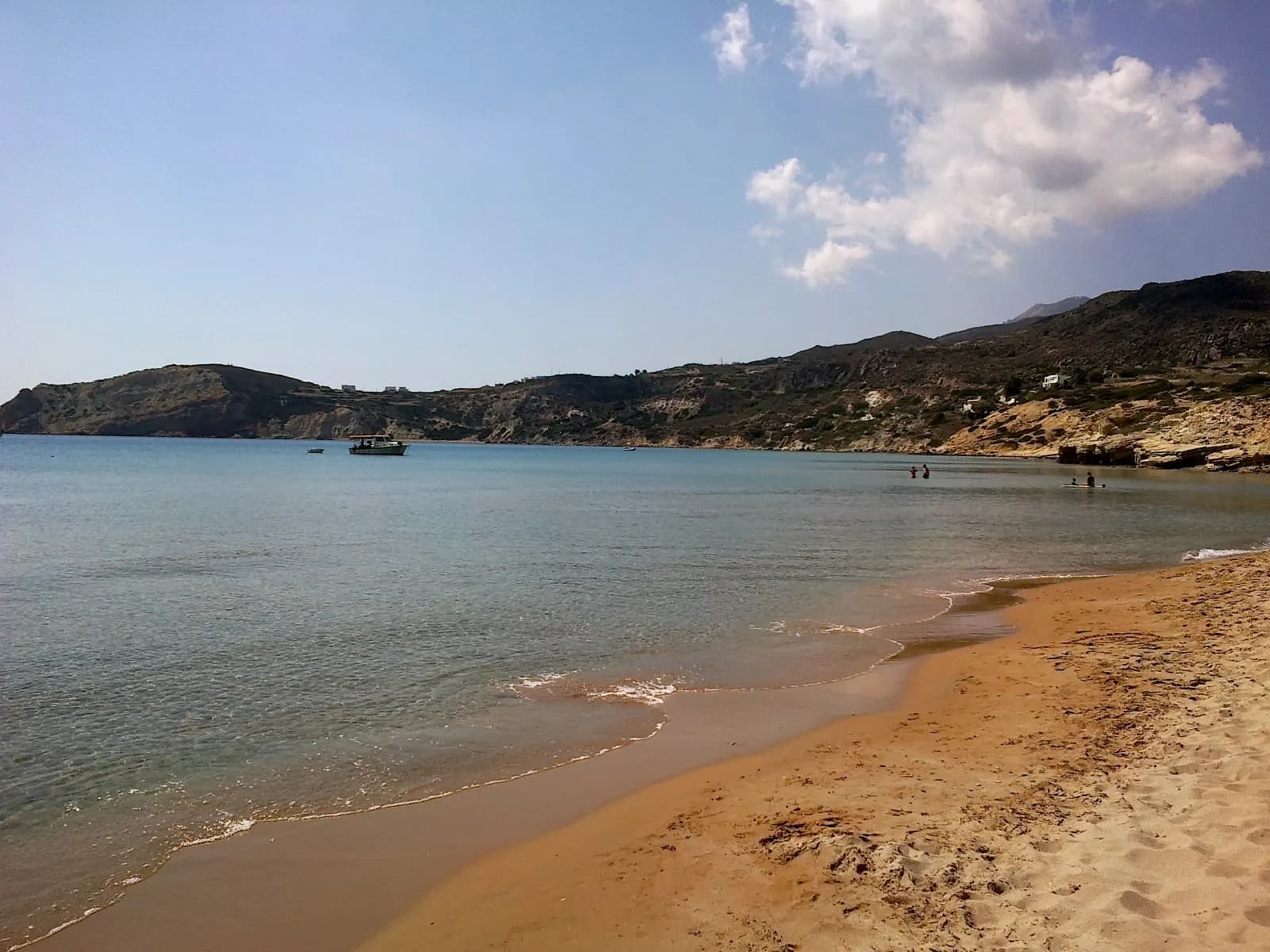 The sandy beach of Provatas with calm water, a moored boat and low hills around the bay