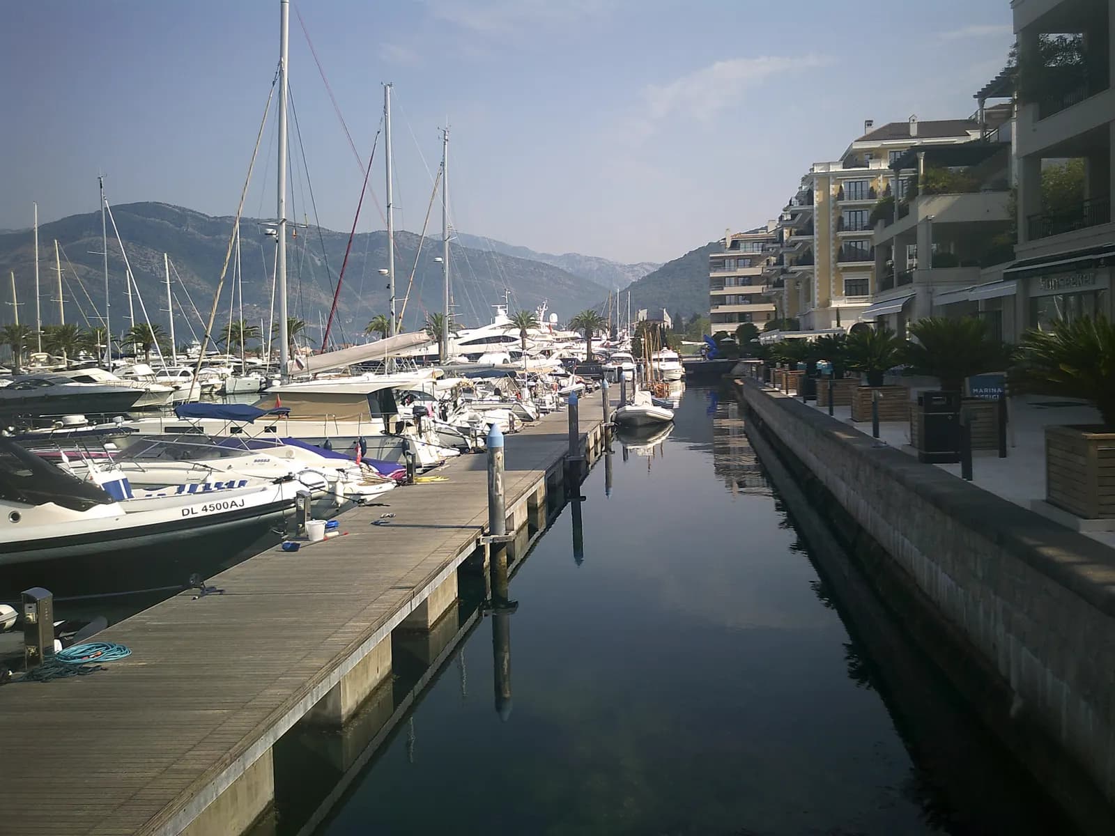 Yachts moored along wooden pontoons in the Porto Montenegro marina in Tivat, with apartment buildings on the quay and mountains behind