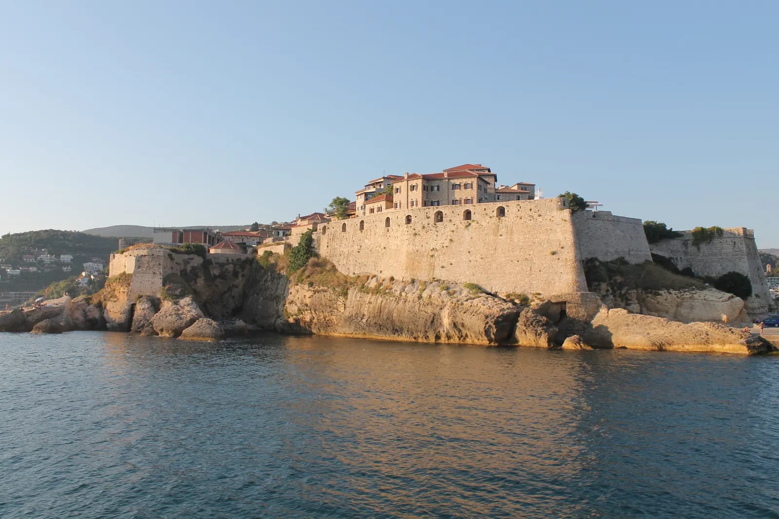 The walls of Ulcinj old town on a rocky headland above the sea, with stone houses behind the ramparts
