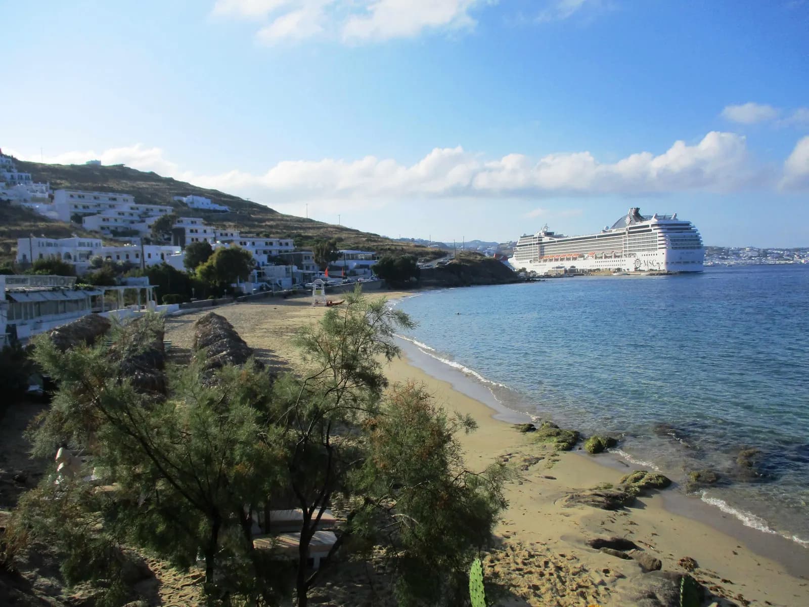 Agios Stefanos beach north of Chora, with tamarisk trees, white hotels on the hillside and a cruise ship moored beyond