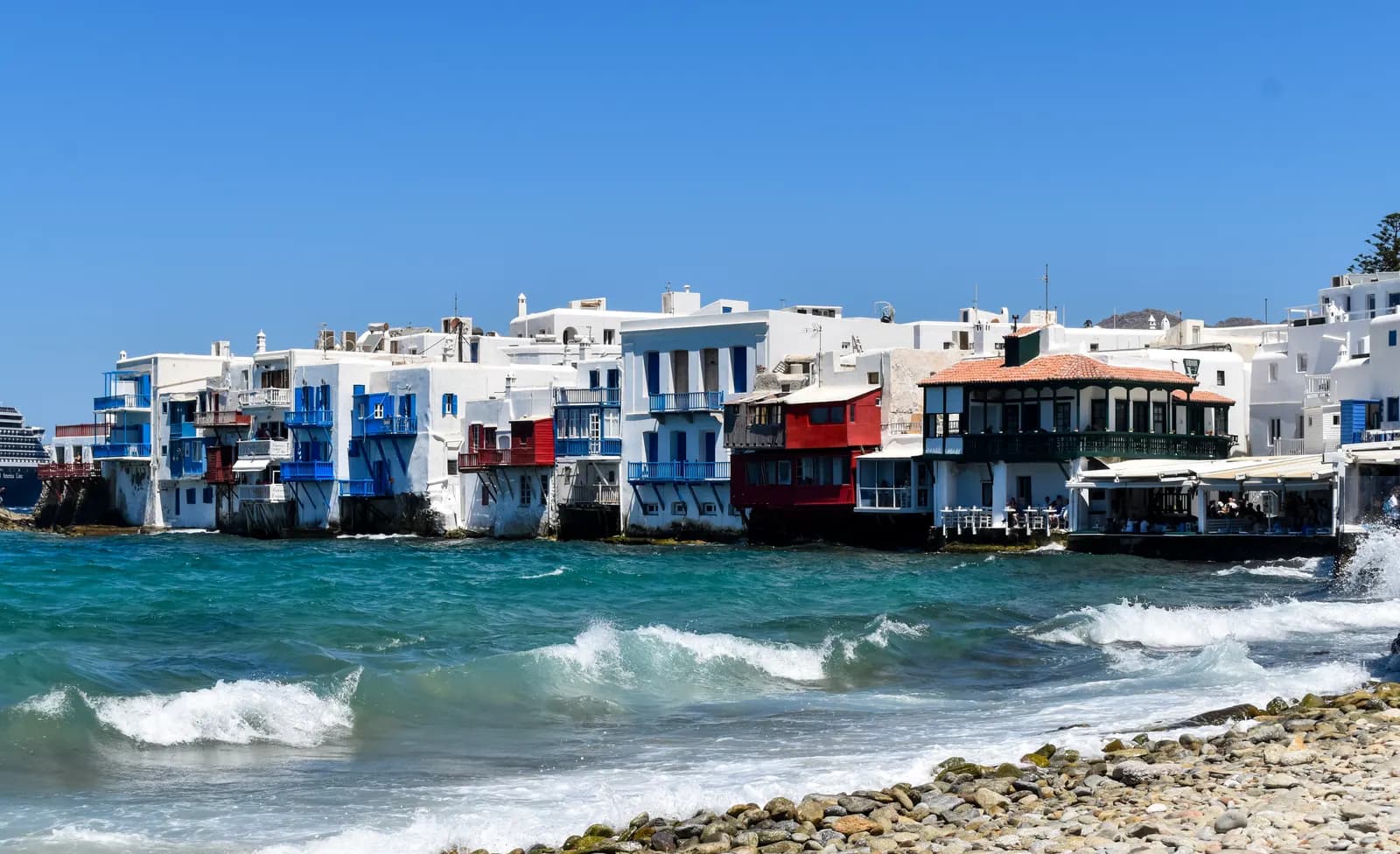 The painted balconies and whitewashed houses of Little Venice in Chora rise straight out of the sea, with waves breaking on the pebble shore in front