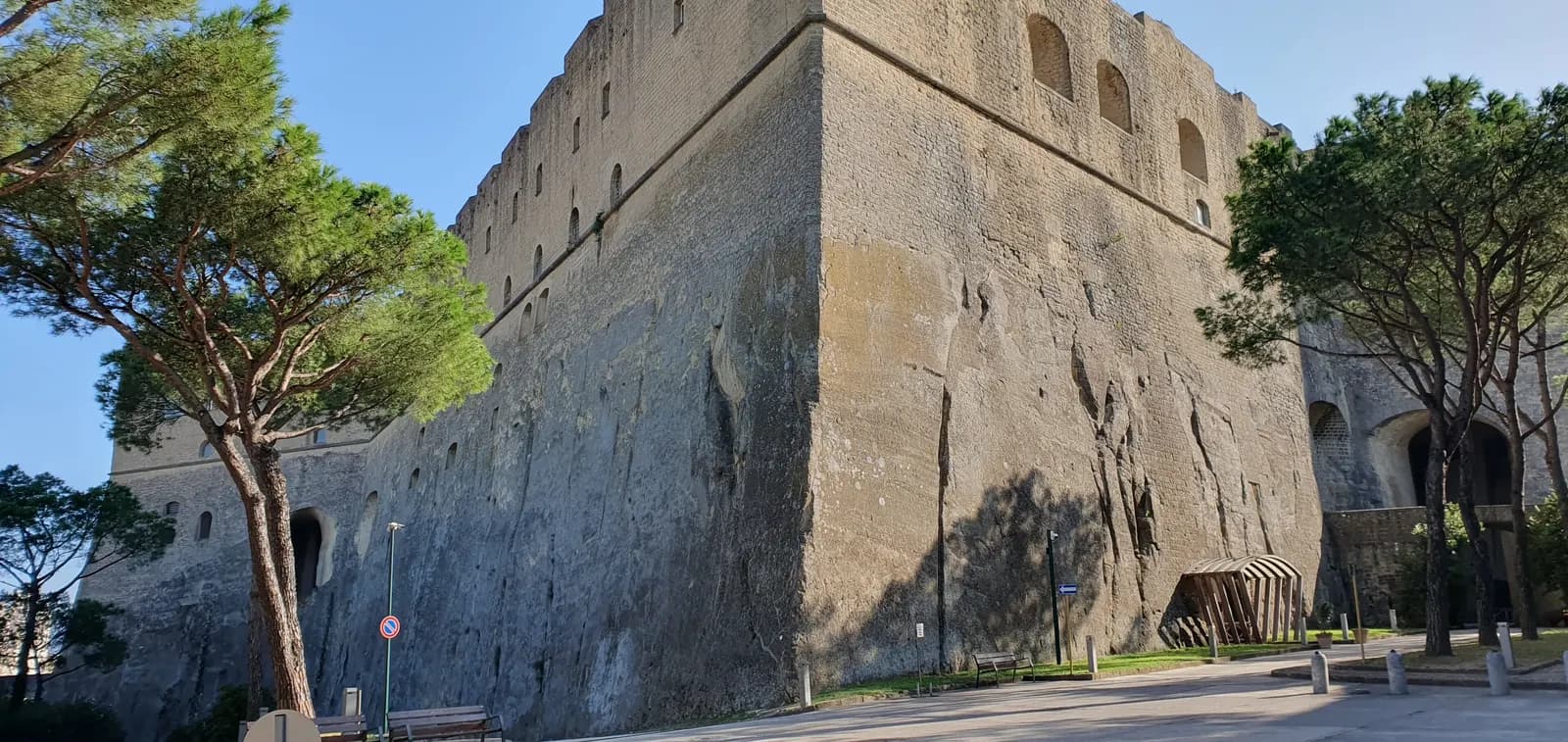 The massive stone walls of Castel Sant'Elmo on the Vomero hill, with umbrella pines and a paved square in front.