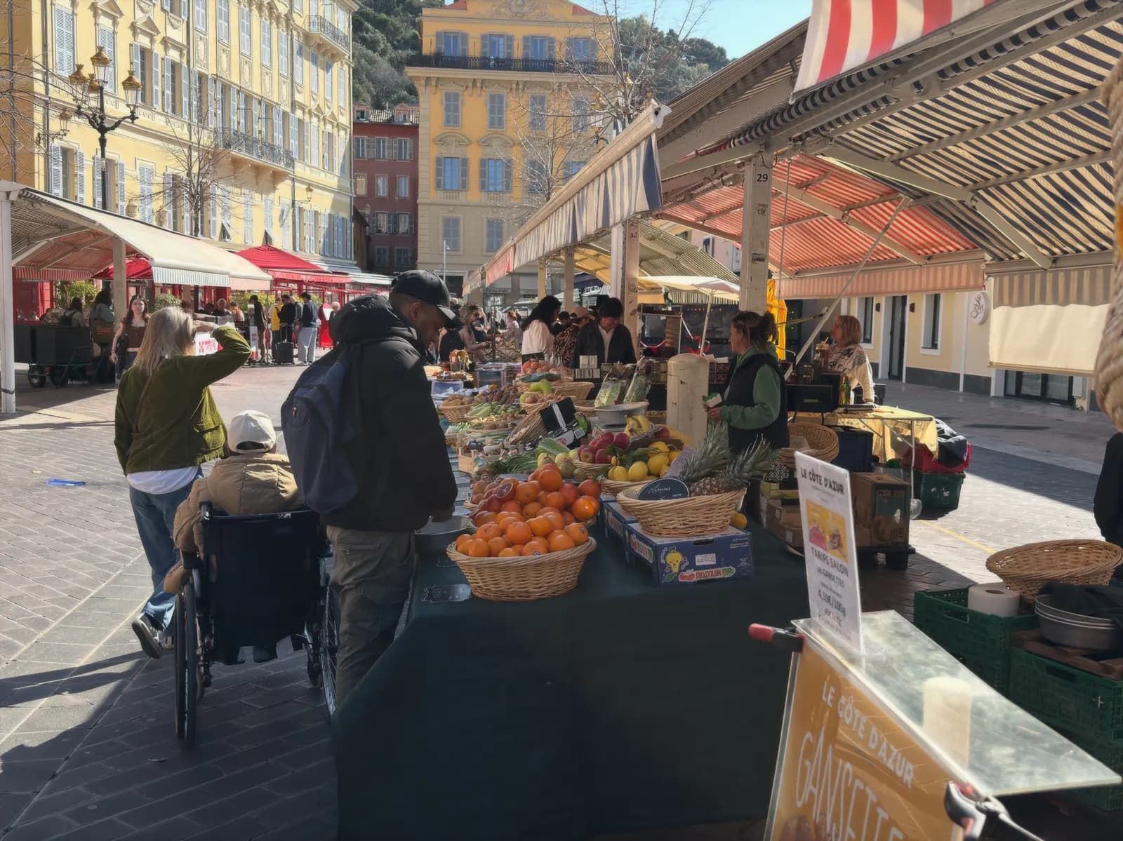 Fruit and vegetable stalls under striped awnings on the Cours Saleya market in the old town of Nice, with ochre and red houses behind