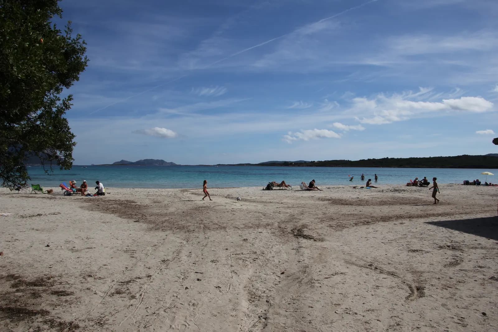 The white sand beach at Porto Istana with clear shallow water, a few people on the sand and low islands on the horizon