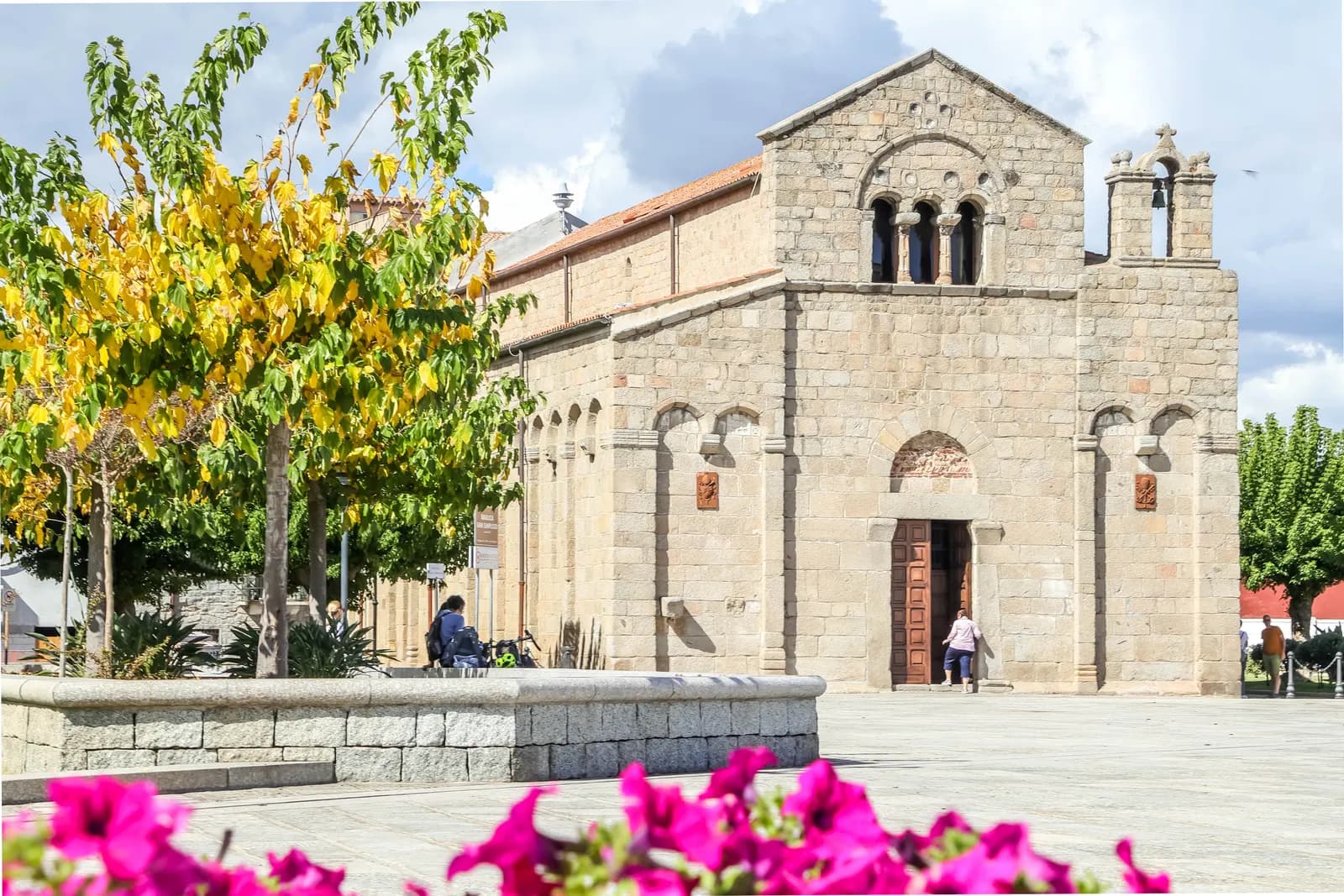 The granite basilica of San Simplicio in Olbia, with its round arched doorway, bell gable and a line of trees in the square in front
