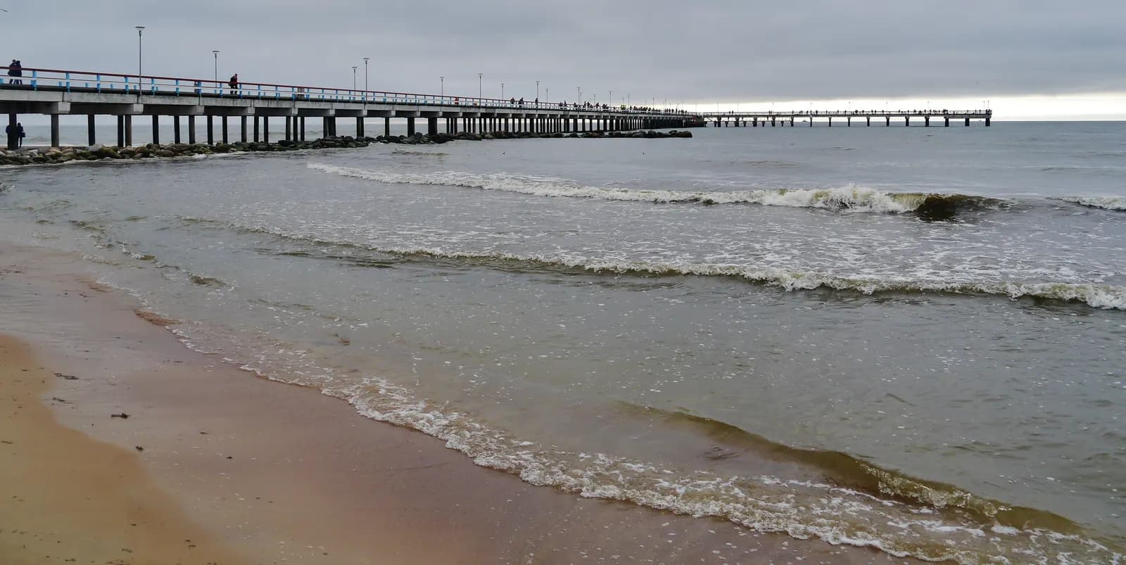 Palanga pier running out into the Baltic Sea, seen from the sandy beach under a grey sky