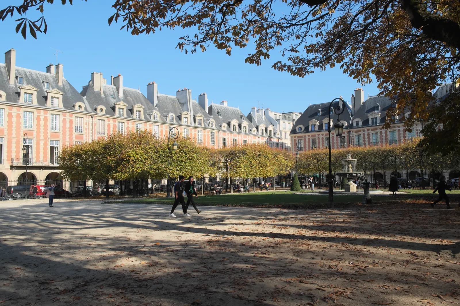 The brick and stone pavilions of the Place des Vosges in the Marais seen across the square's gravel and clipped trees in autumn