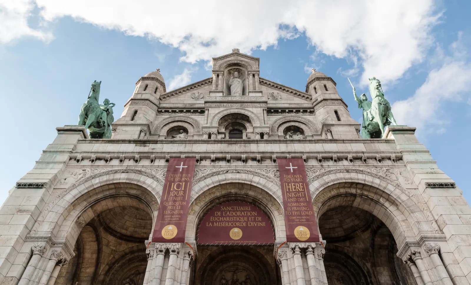 The west front of the Sacré-Cœur basilica on Montmartre seen from below, with the equestrian statues and the three entrance arches