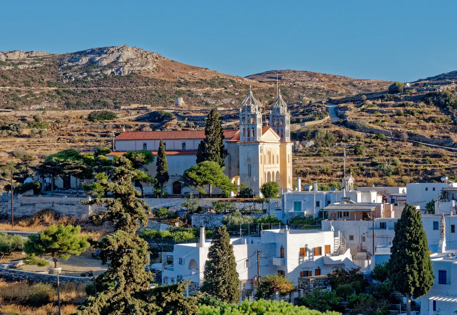 The white houses of Lefkes below the twin bell towers of the church of Agia Triada, with terraced hills behind