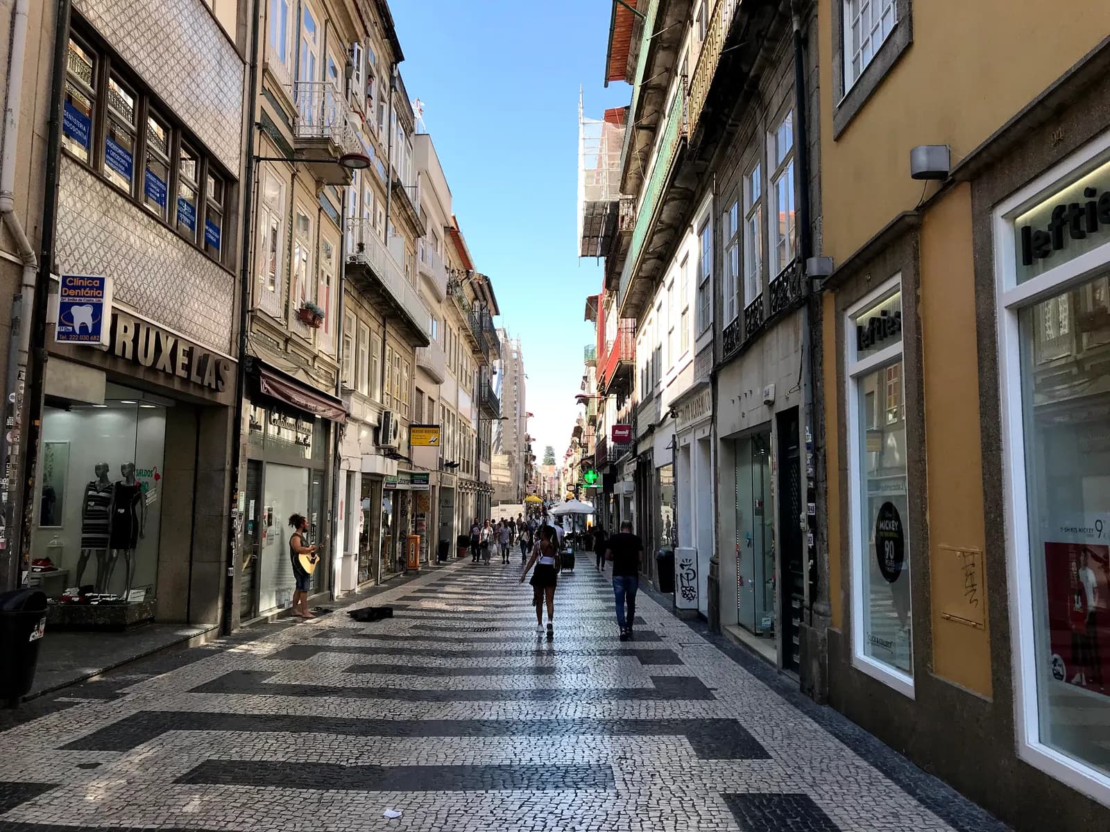 Pedestrian Rua de Cedofeita with patterned cobbles, shopfronts and people walking between tall town houses.