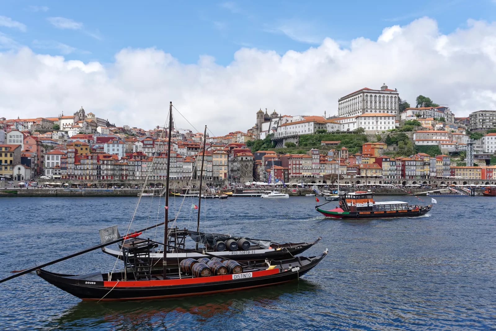 Traditional rabelo boats on the Douro in front of the Ribeira waterfront, with Porto Cathedral and the Bishop's Palace on the hill above.
