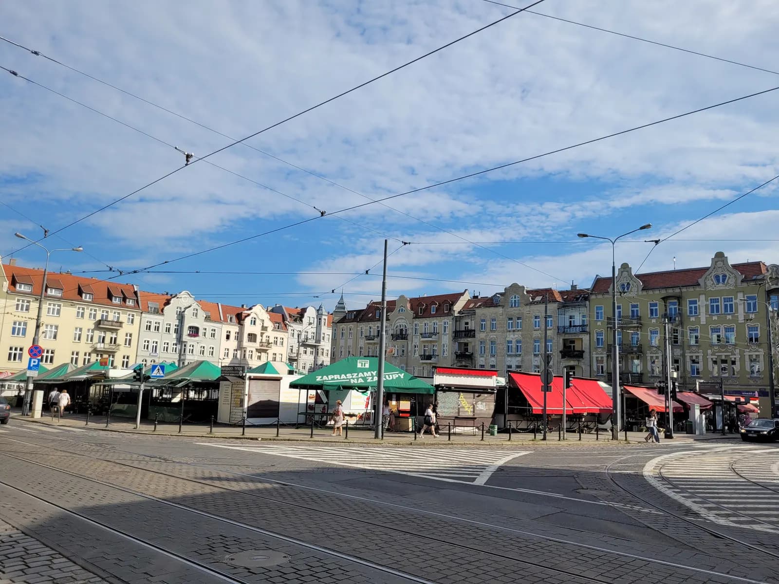 Rynek Jeżycki in Poznań, a market square with green and red stall awnings, tram tracks and overhead wires in front of a row of tenements