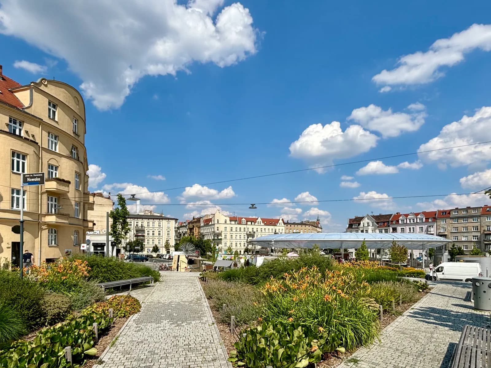 Rynek Łazarski in Poznań, a square with paved paths through flower beds, tenements around it and a long glass canopy in the distance