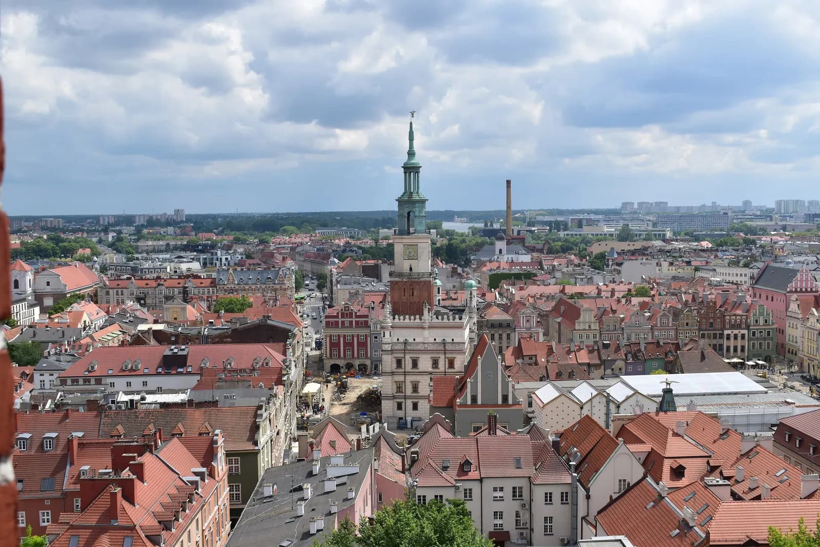 Red tiled rooftops of Poznań's Old Town seen from above, with the slender green-topped tower of the Town Hall rising in the middle