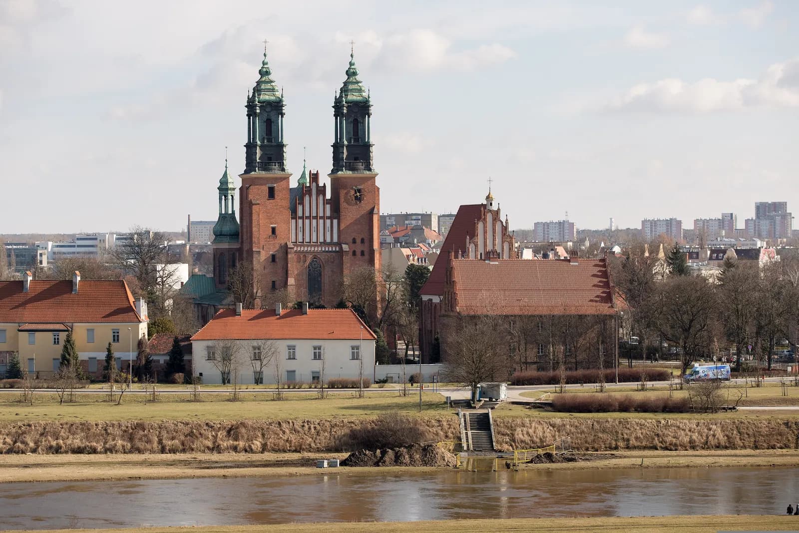 Poznań Cathedral with its two green-capped towers on Ostrów Tumski, seen across the river with low red-roofed buildings in front