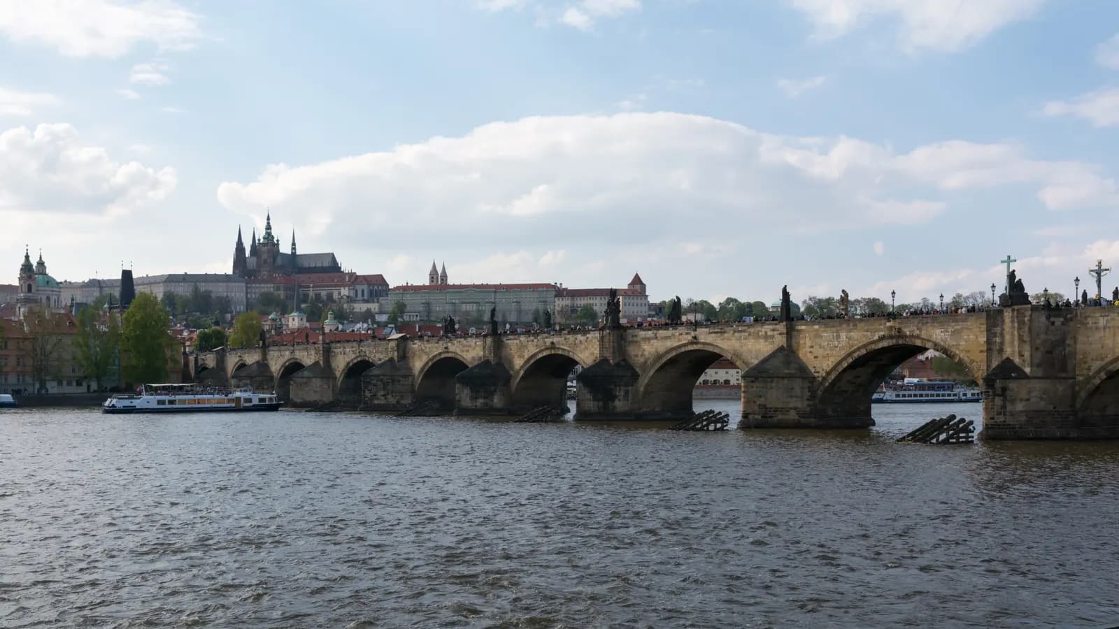 Charles Bridge crossing the Vltava in Prague on a sunny day, with Prague Castle and St Vitus Cathedral on the hill behind