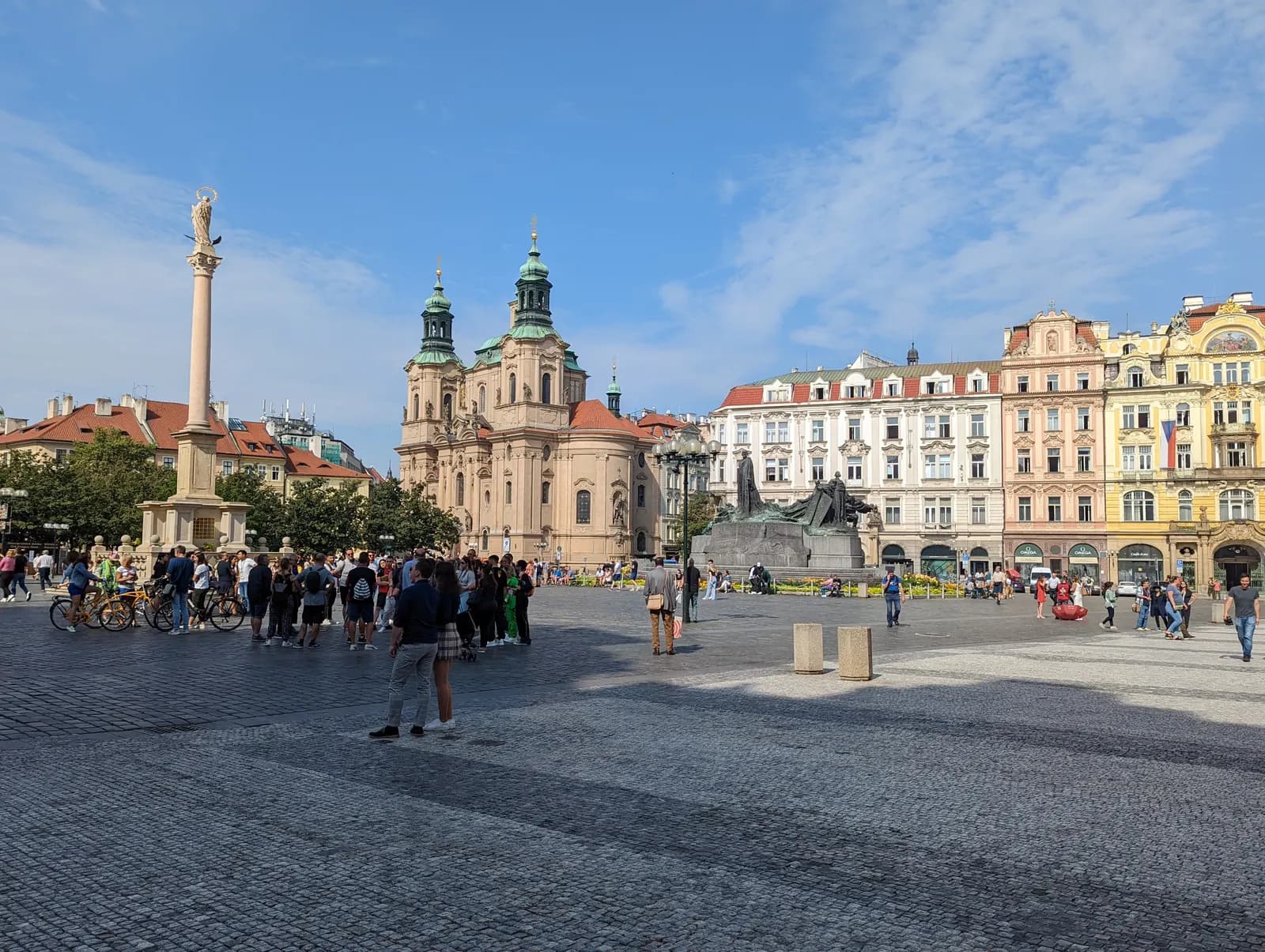 Old Town Square in Prague with the Marian column, the Baroque Church of St Nicholas, the Jan Hus monument and pastel house fronts under a blue sky
