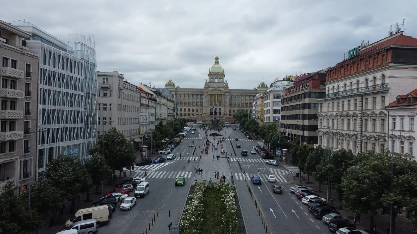 Wenceslas Square in Prague seen from above, a long boulevard with trees and parked cars leading up to the National Museum