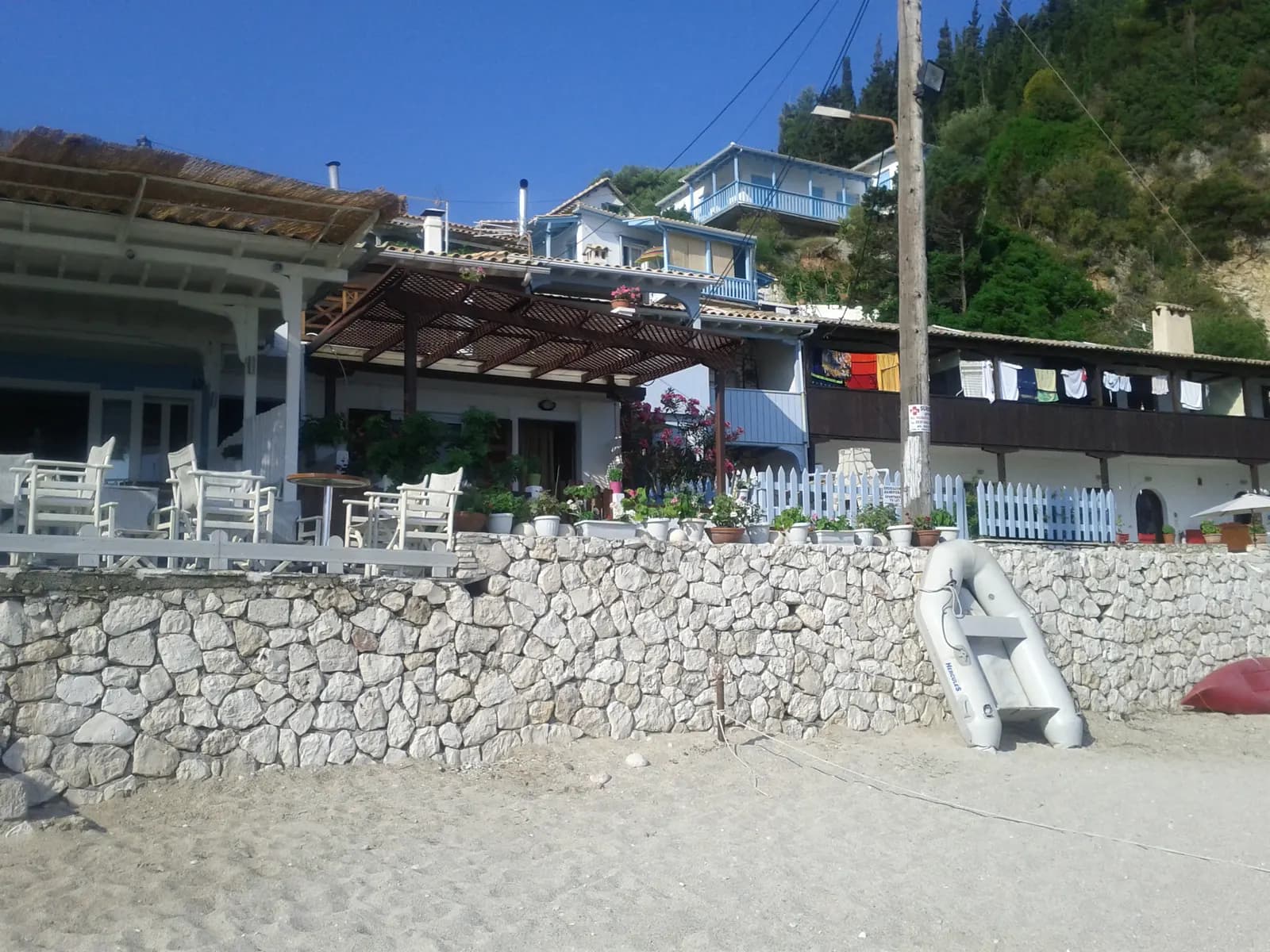 Houses and tavernas with wooden balconies above a stone sea wall at the back of the sandy beach in Agios Nikitas, with a small dinghy on the sand