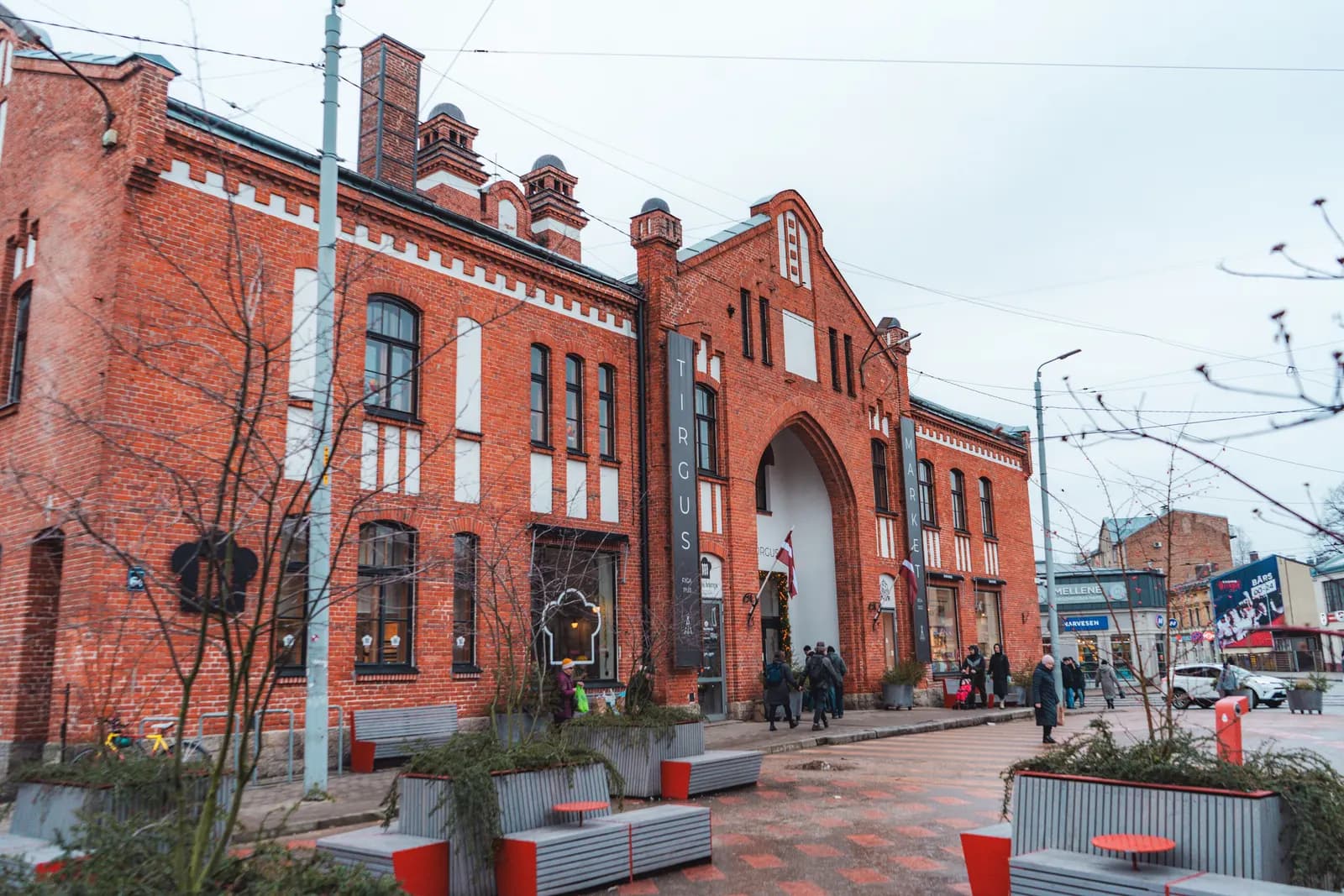 The red-brick Āgenskalns Market hall in Riga with its arched entrance and benches on the square in front