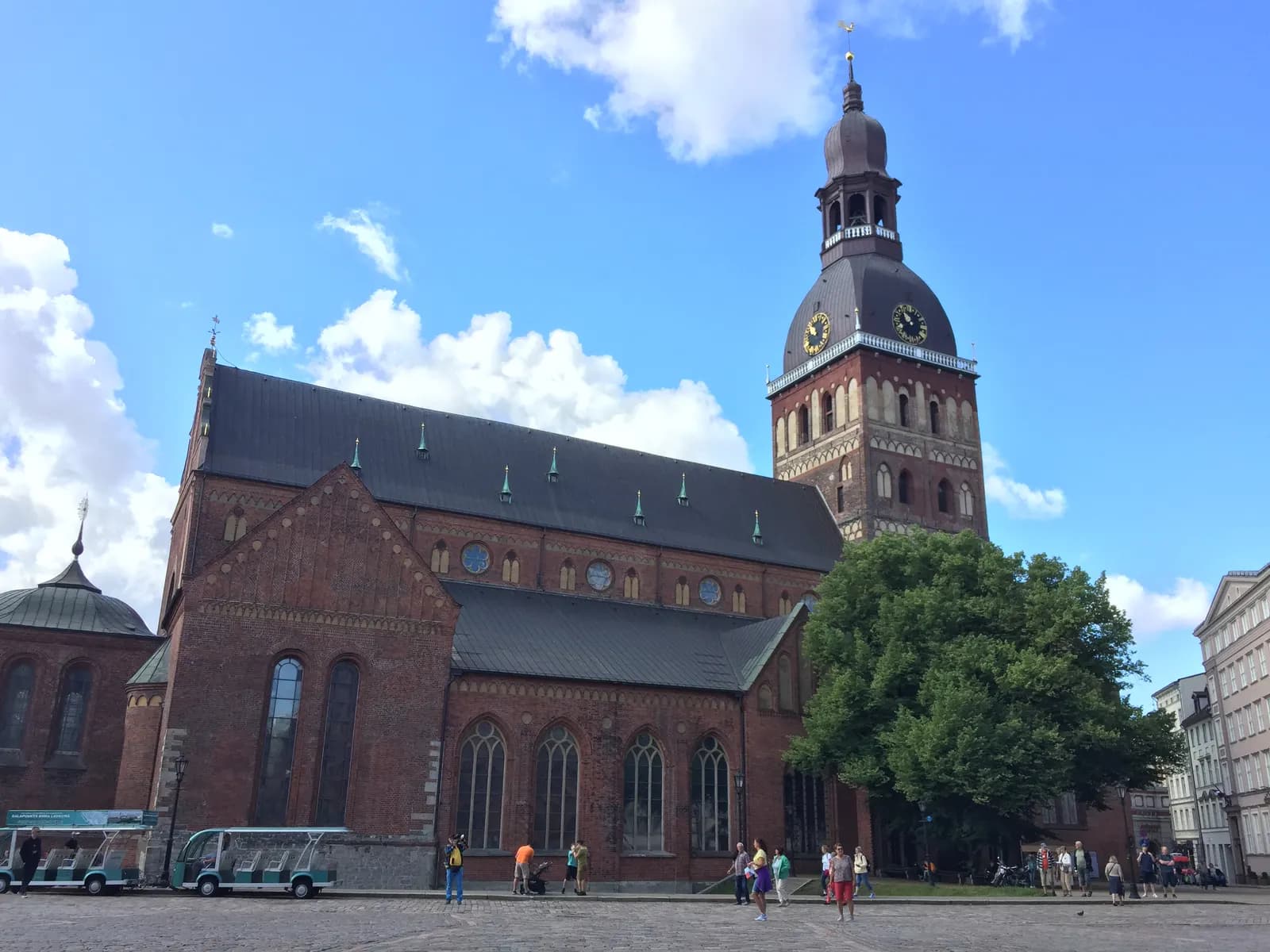 The brick nave and tower of Riga Cathedral on Dome Square, with visitors and electric tour carts in front