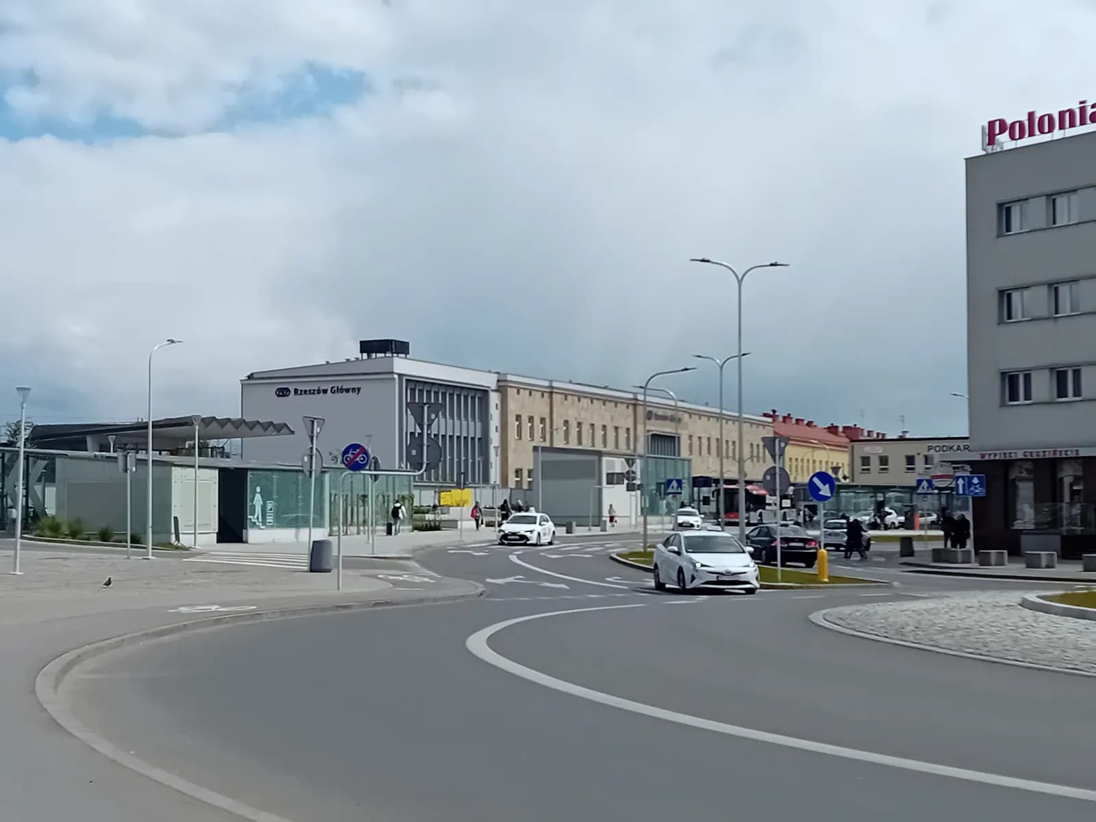 The Rzeszów Główny railway station building seen across a roundabout, with cars and the Polonia building on the right