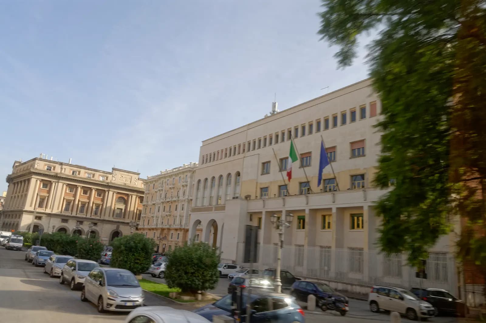 Cars parked along both sides of a wide street in central Salerno in front of the Palazzo della Prefettura, with the older Palazzo di Citta beyond it.