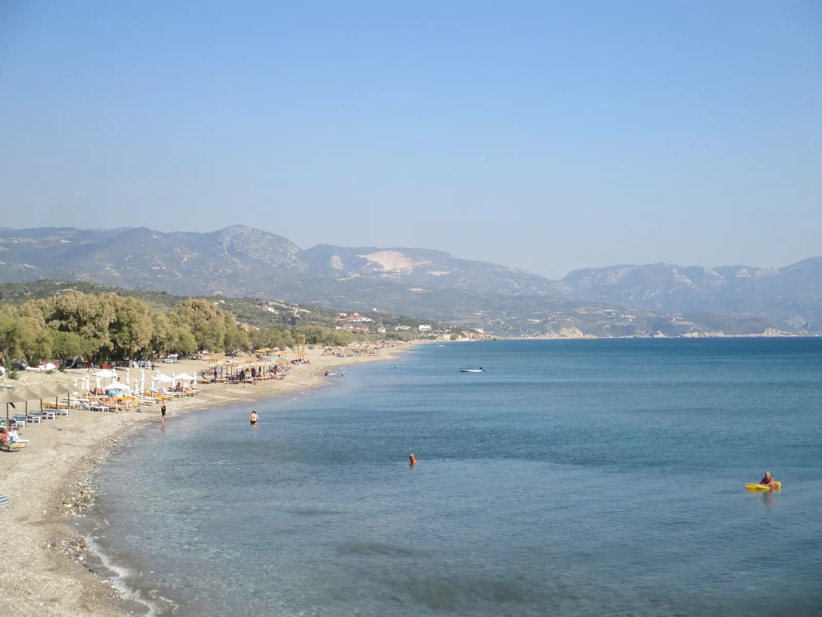 The long pebble and sand beach at Kampos (Votsalakia) with umbrellas, tamarisk trees and mountains behind
