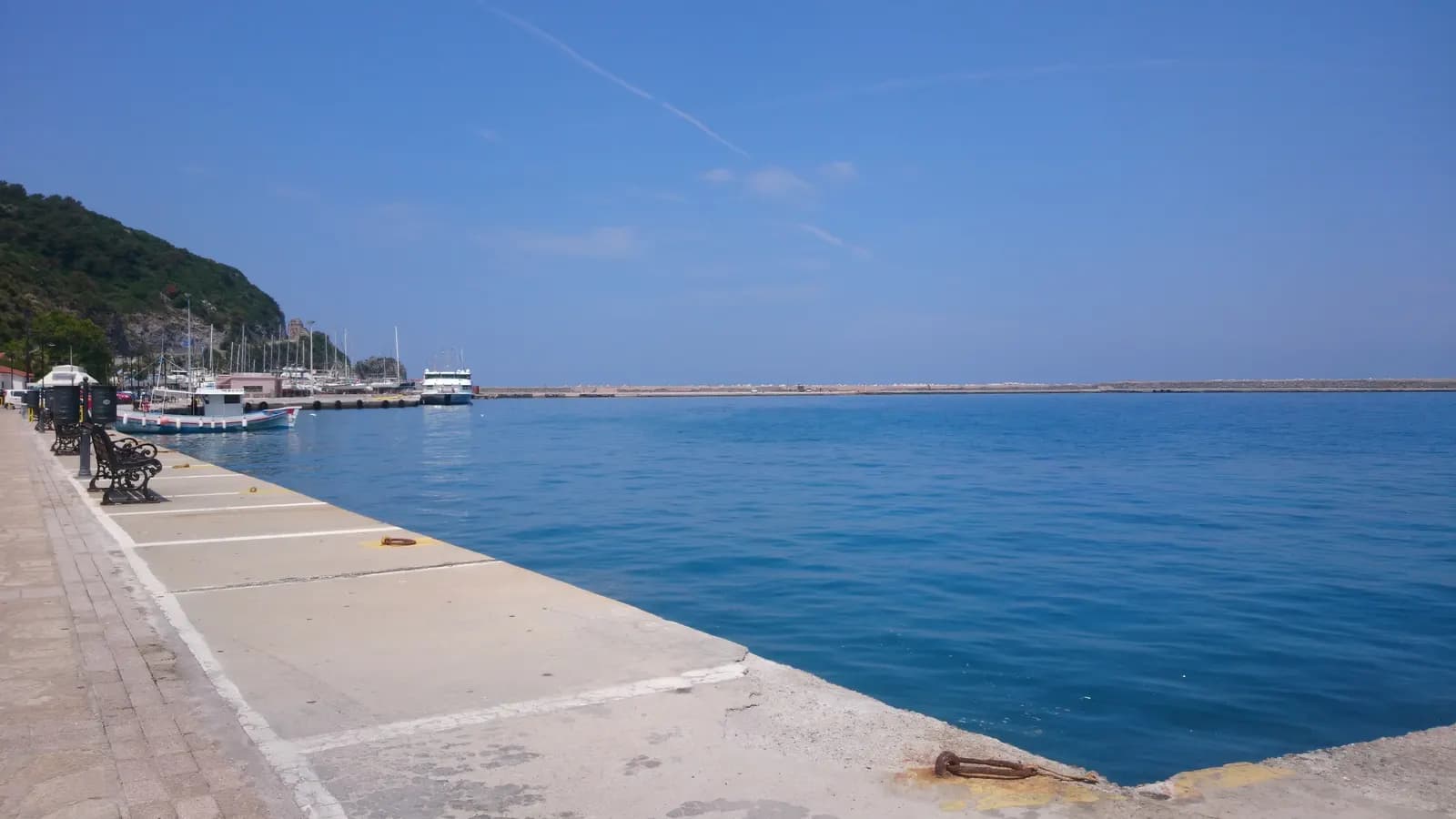 The quay at Karlovasi port with benches, fishing boats and a ferry at the far end of the harbour