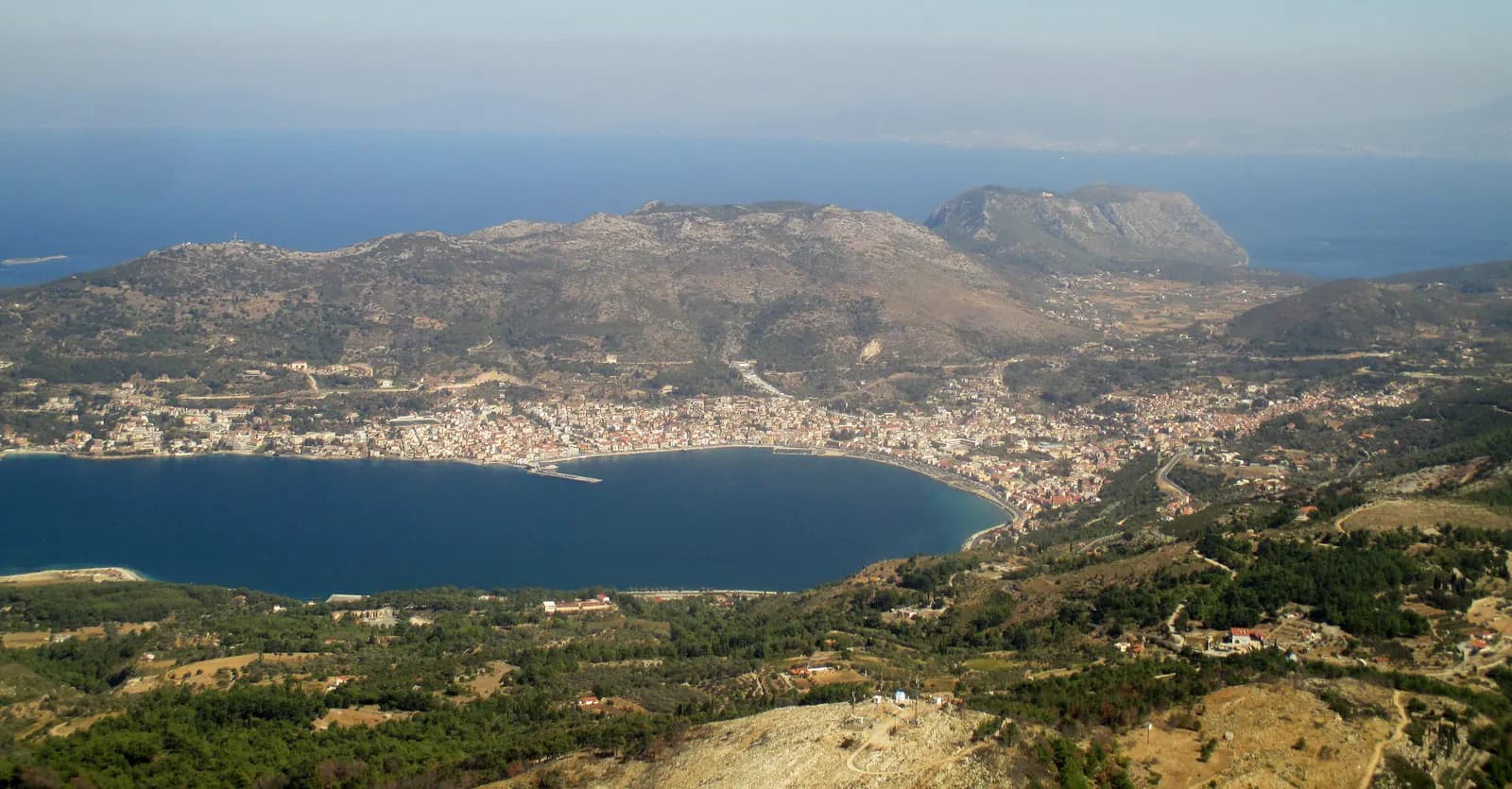 Samos town spread around the curve of Vathy bay, seen from the mountains above, with the sea and distant coastline beyond