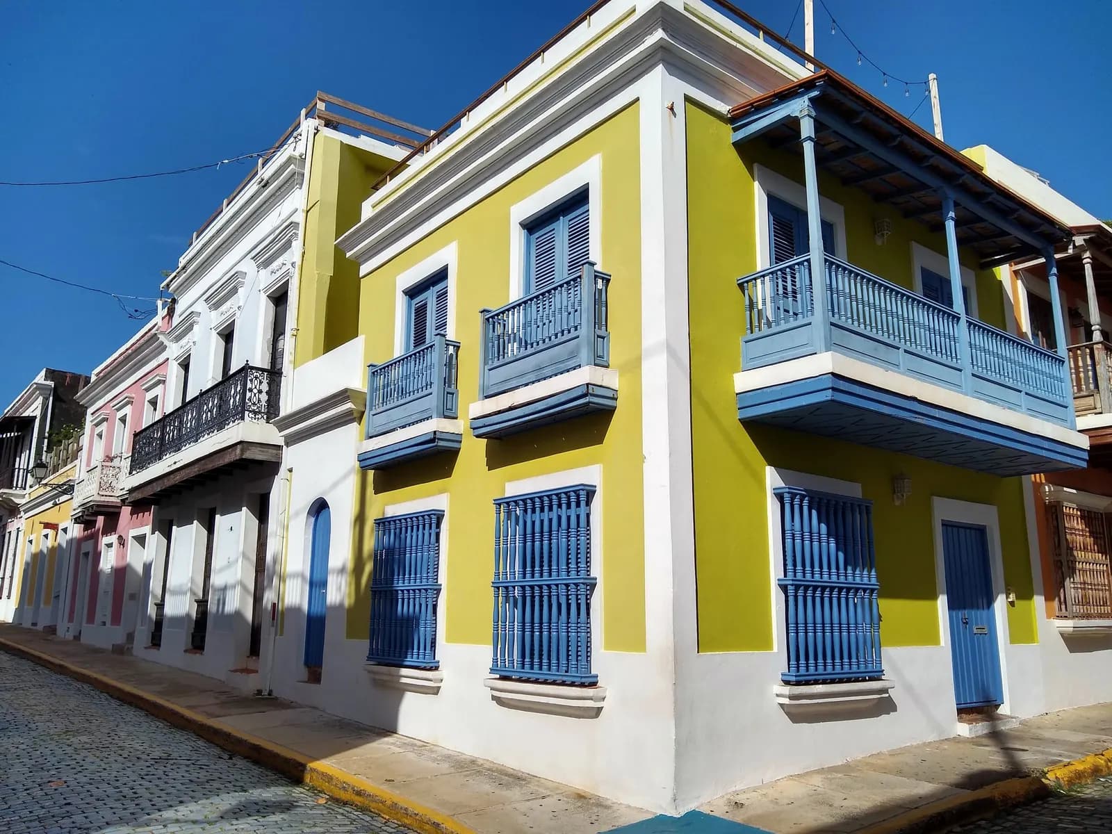 A yellow colonial house with blue wooden balconies and window grilles on a cobbled street corner in Old San Juan
