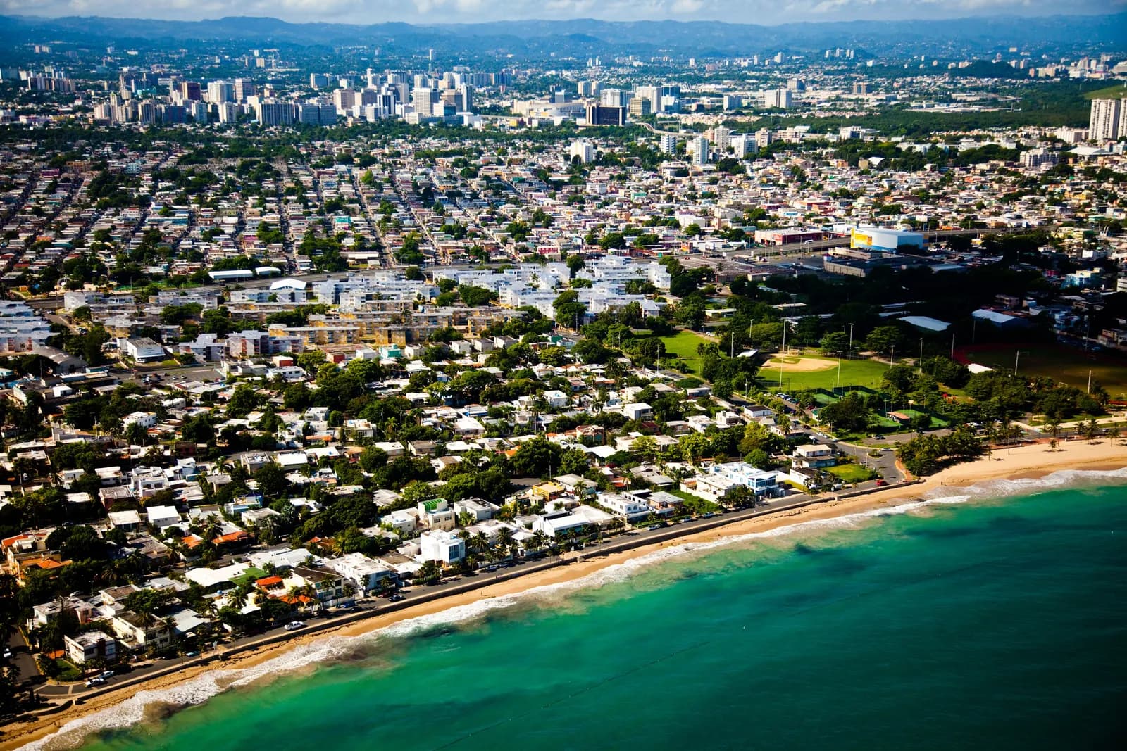 Aerial view of Ocean Park in San Juan, with low houses along a sandy beach and the towers of the city behind