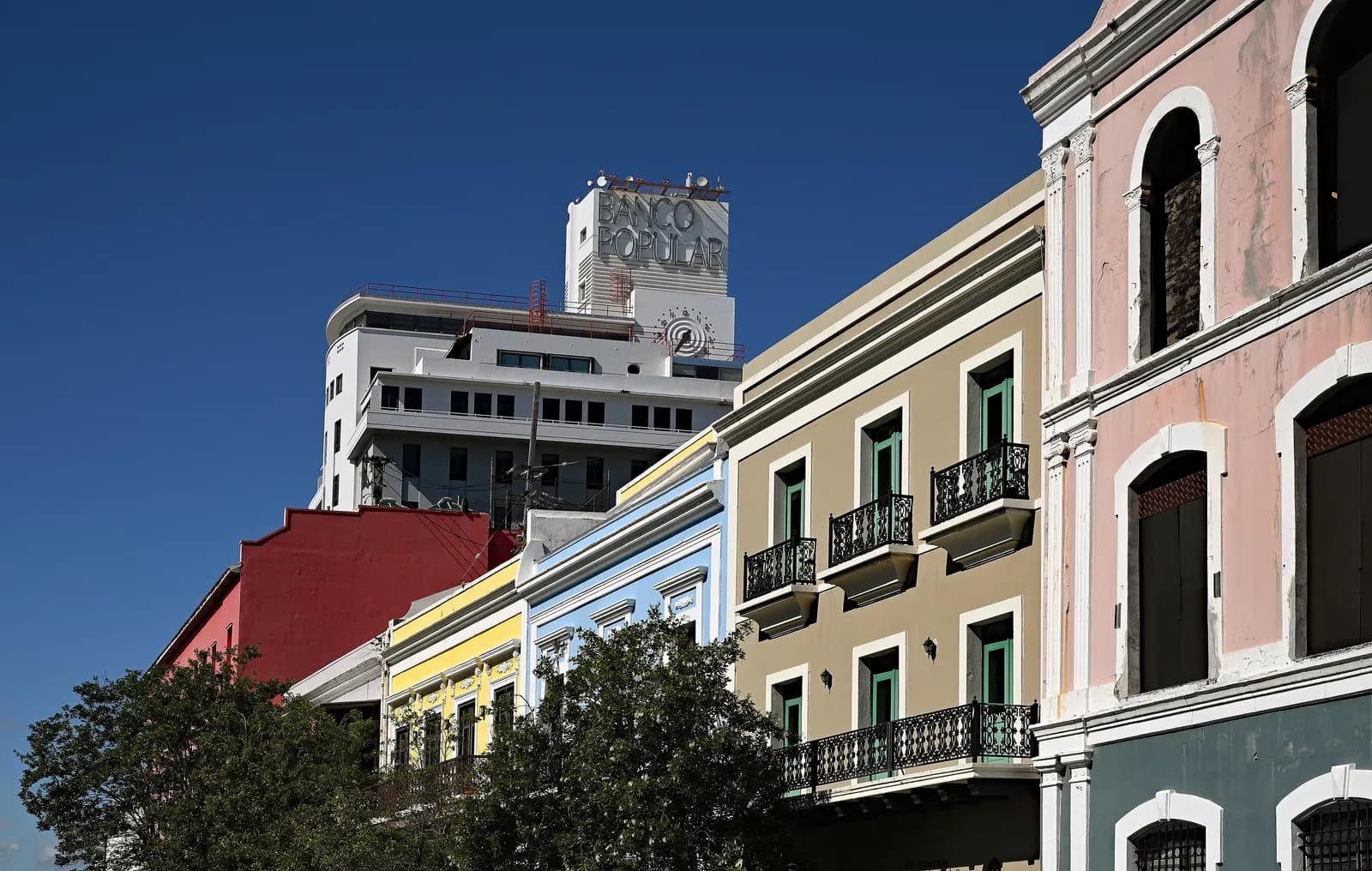 Pastel-coloured buildings with iron balconies along Recinto Sur Street in Old San Juan, with a white bank tower behind
