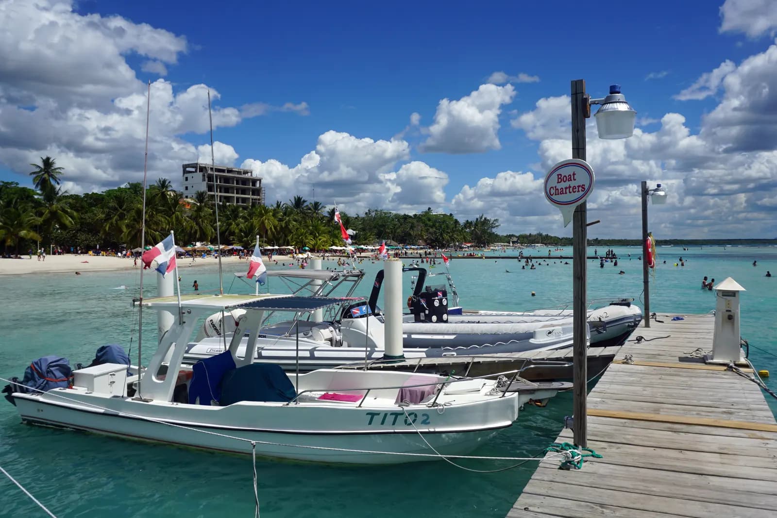 Boats moored at a wooden jetty at Boca Chica, with swimmers in the shallow turquoise water and the palm-lined beach behind