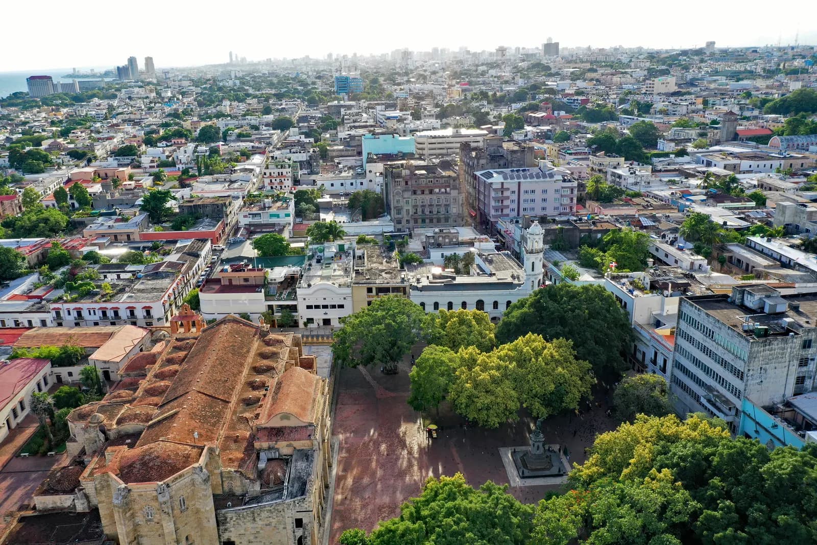Aerial view of the Colonial City of Santo Domingo, with the stone roof of the cathedral, the trees of Parque Colón, the white Palacio Consistorial and the city behind
