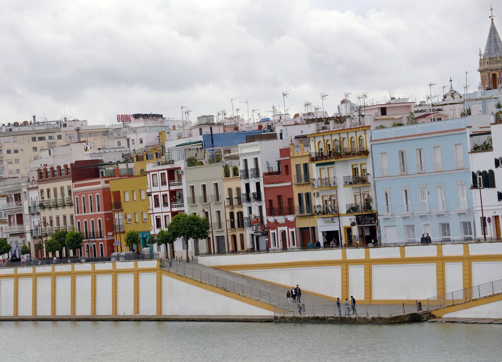 The painted houses of Calle Betis in Triana seen across the Guadalquivir, above the riverside embankment.
