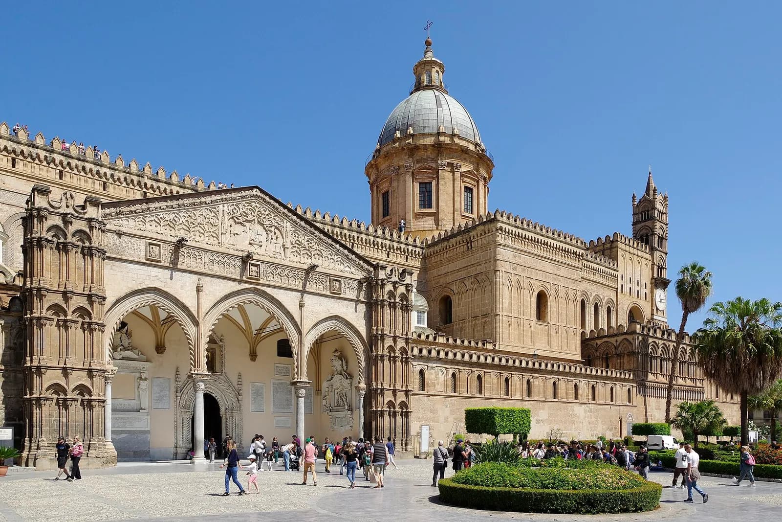 The south side of Palermo Cathedral with its Gothic portico, dome and bell towers, and visitors crossing the square in front