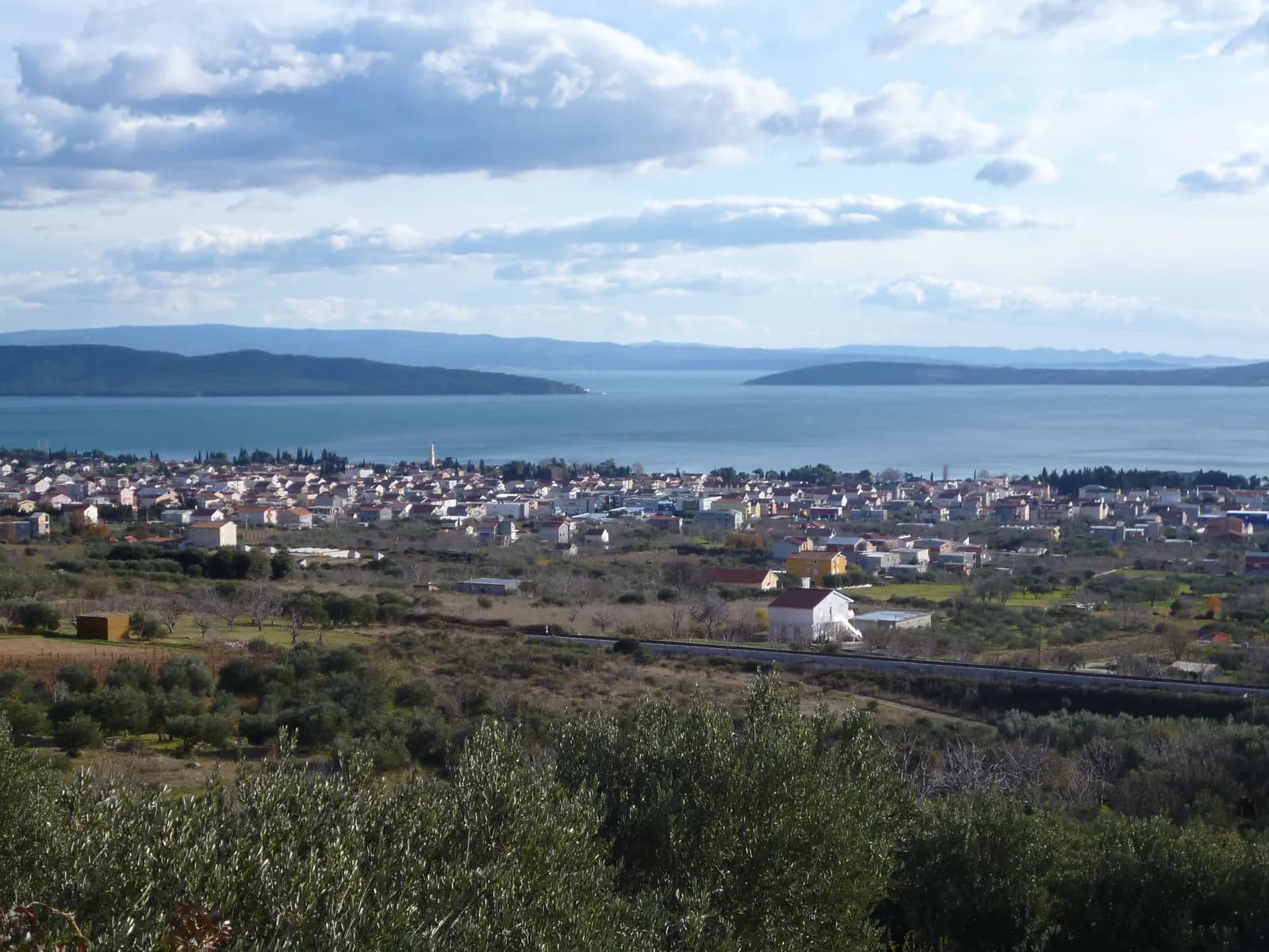 Houses of Kaštel Lukšić spread along the Bay of Kaštela, seen from the Kozjak slopes above olive groves