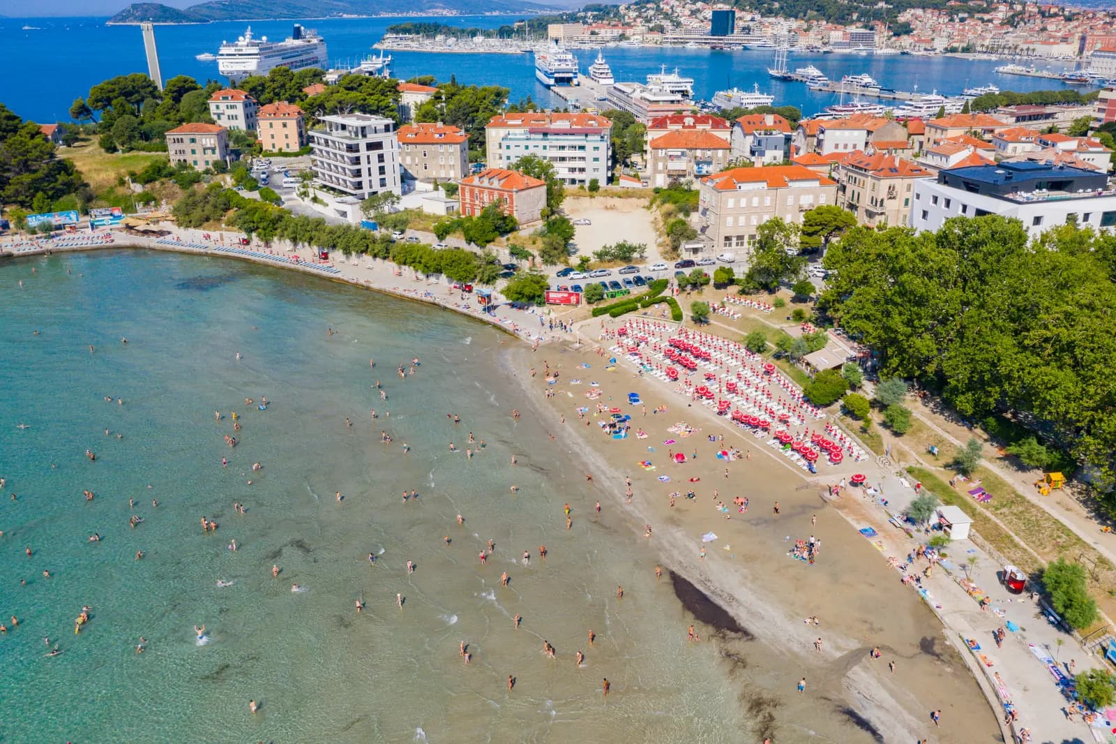 Aerial view of the shallow sandy Bačvice beach in Split with swimmers, sunshades and the city and ferry port behind