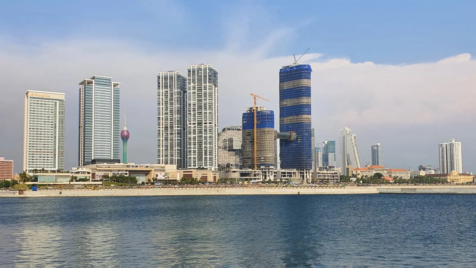 The Colombo skyline seen across the water from the Port City, with high-rise towers and a tower under construction beside a crane