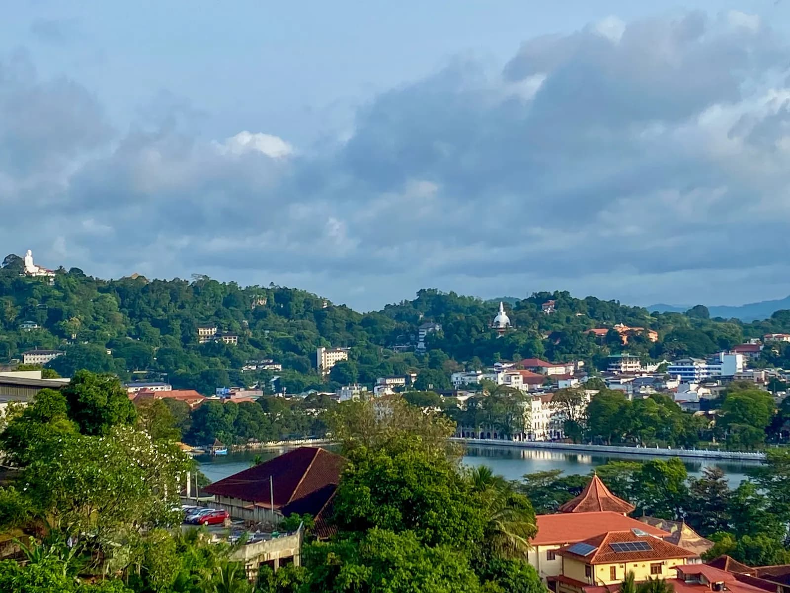 Kandy Lake seen from a hillside, with the Temple of the Sacred Tooth Relic beyond it, buildings along the shore and wooded hills behind