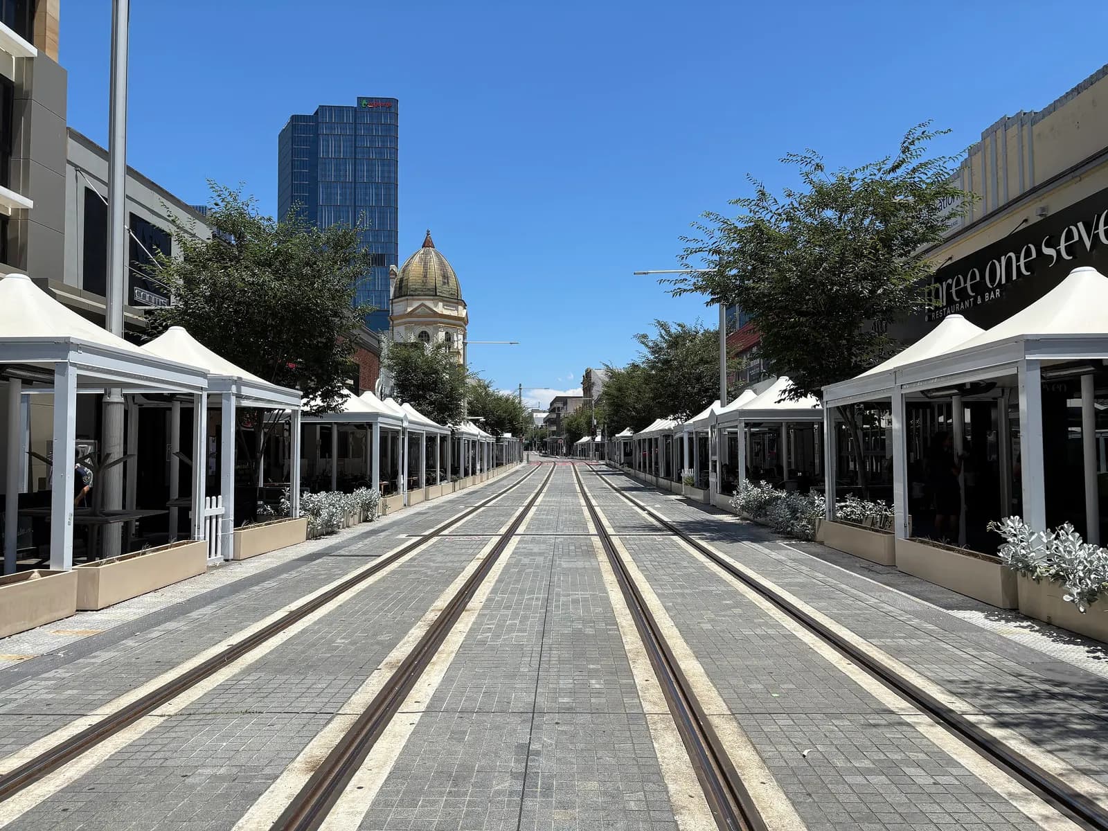 Church Street in Parramatta with light rail tracks between rows of white outdoor dining pavilions, and a domed old building and an office tower behind