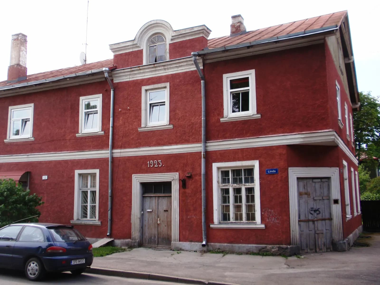 A red two-storey house dated 1923 on the corner of Linda street in Kalamaja, with a car parked in front