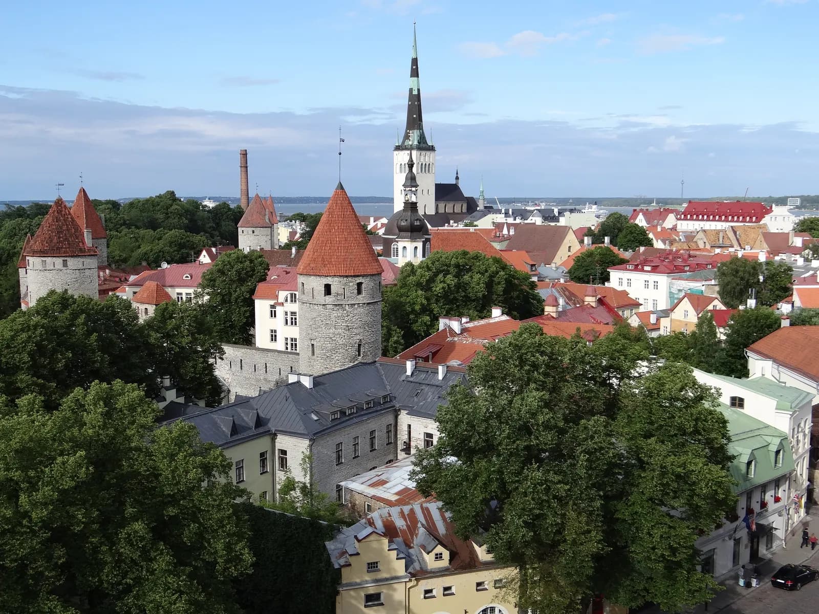 Tallinn Old Town seen from Toompea: medieval towers with red conical roofs, the town wall and a tall church spire above the rooftops
