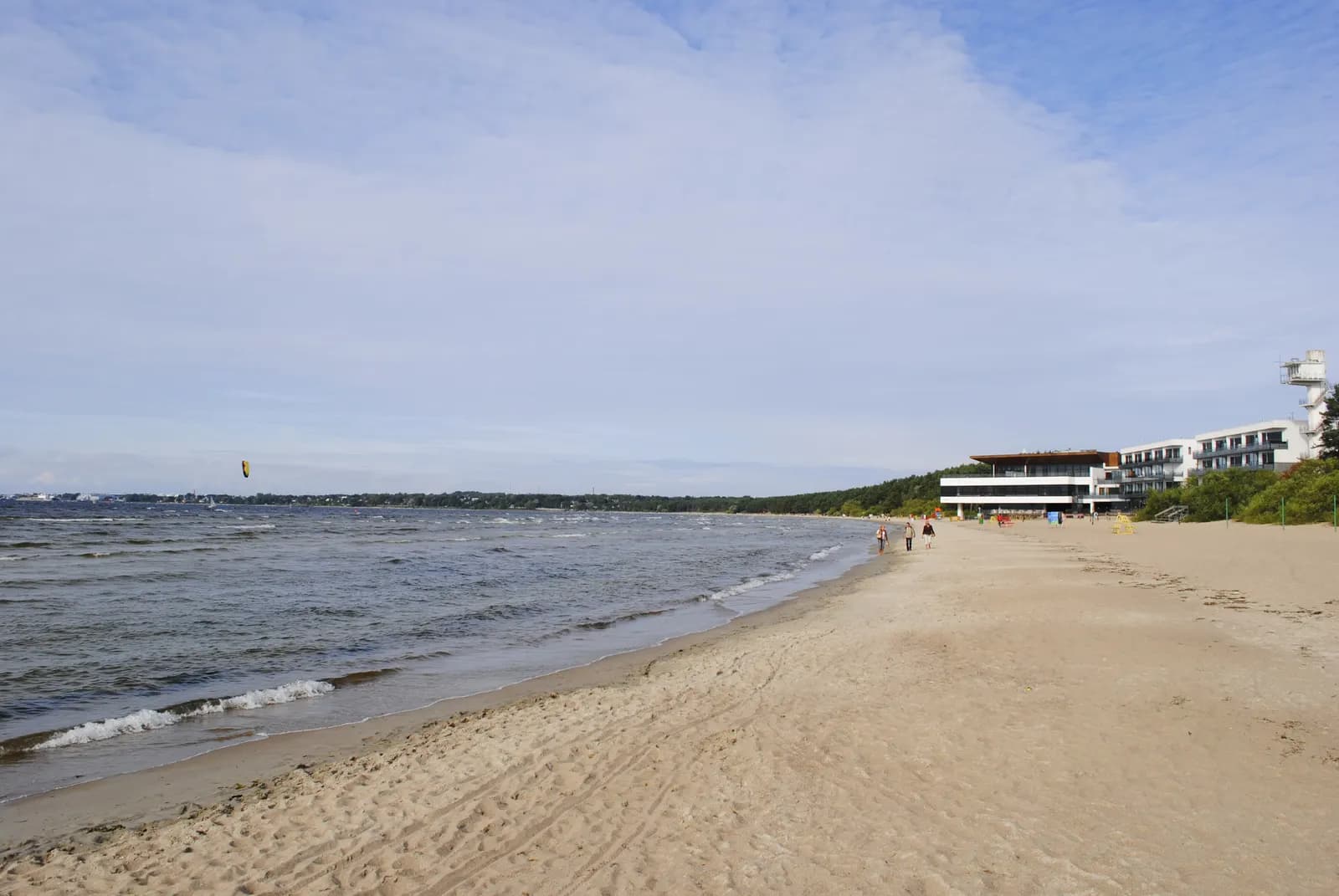 The sandy beach at Pirita in Tallinn, with small waves from the bay and a low modern building at the far end