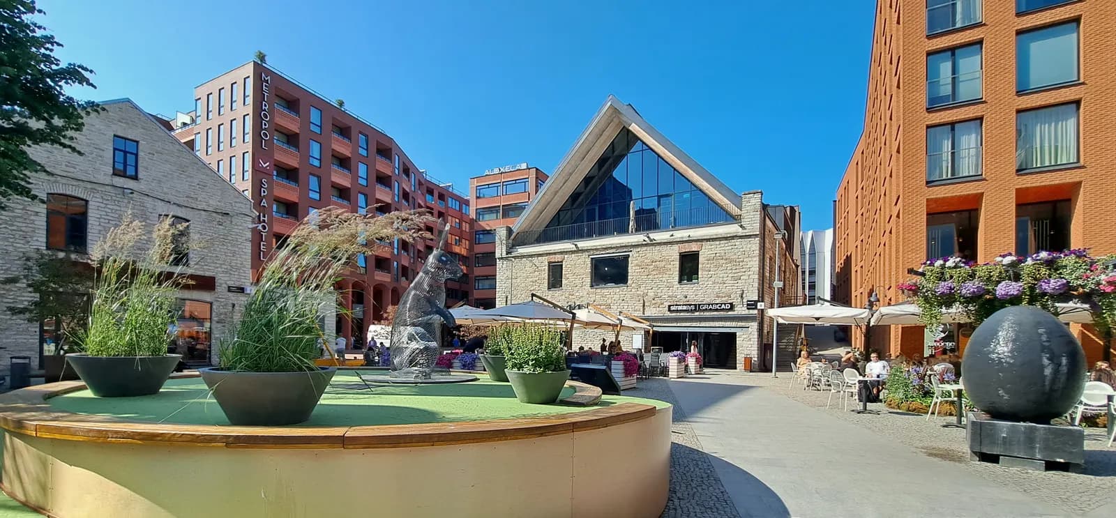 Rotermann Quarter in central Tallinn: a limestone building with a glass gable between new brick blocks, with café tables and planters