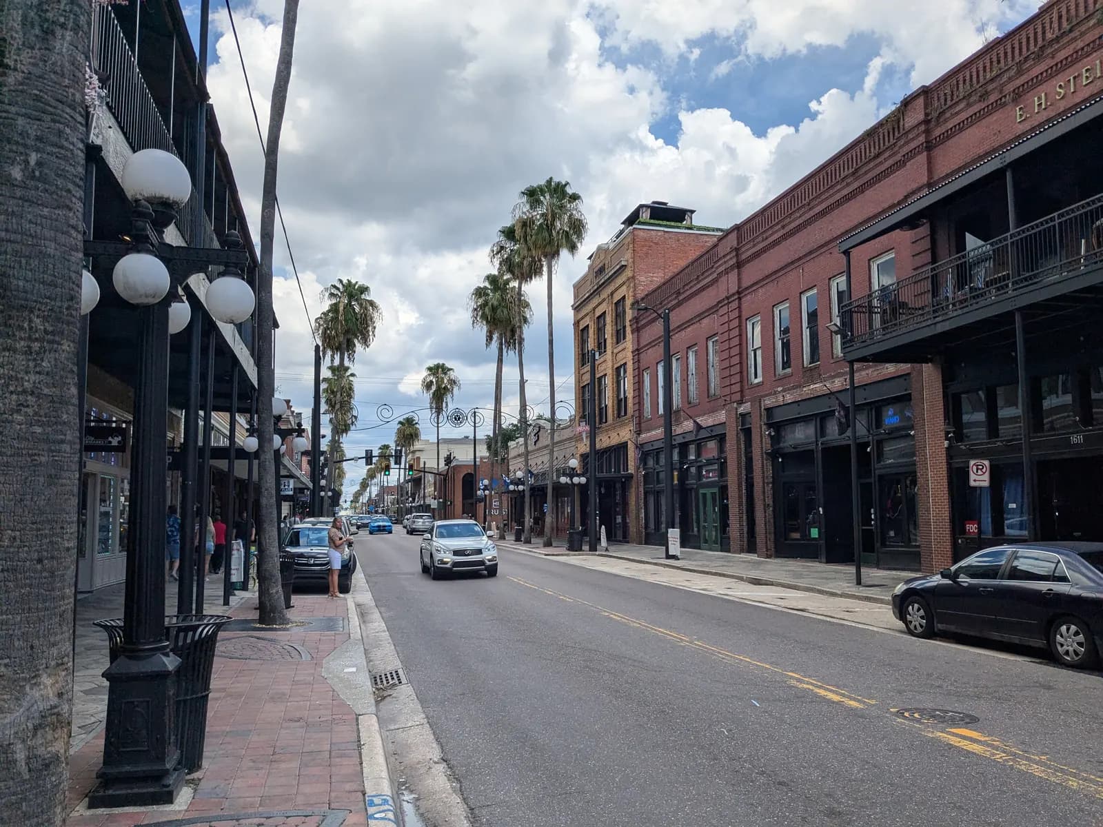 Seventh Avenue in Ybor City, lined with red brick buildings with iron balconies, globe street lamps and tall palm trees, with cars parked along the street