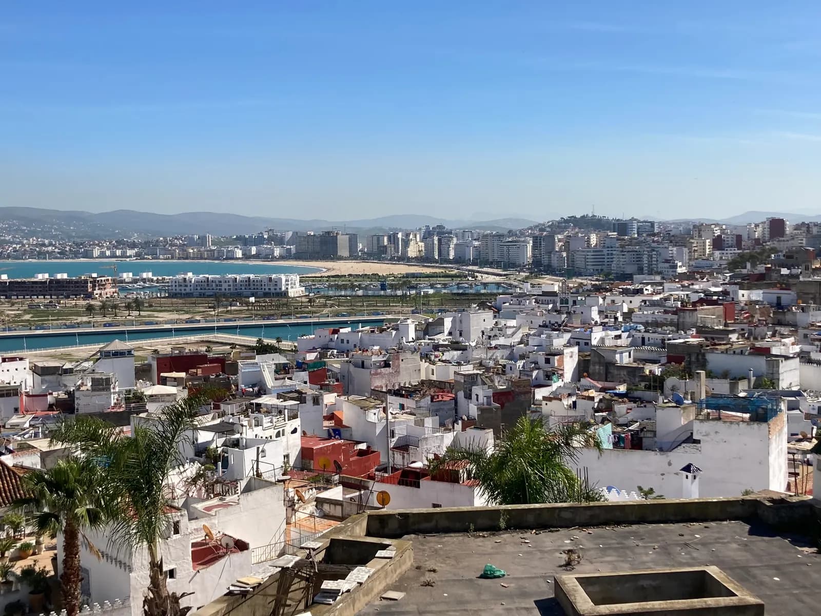 Tangier seen from the Kasbah: white medina rooftops in front, the marina and the long sandy beach of the bay behind, and the modern city rising towards the hills